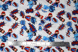 Flat swatch of cartoon superhero print pattern in blue (white fabric with grey polka dots, cartoon superhero characters in blue, black and red colourway with comic book style words and logos "POW!" etc)