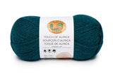 A ball of Lion Brand Touch of Alpaca yarn in jade shade on white background (deep peacock teal blue)