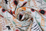 Swirled swatch Words fabric (cream fabric with fall related text and emblems allover in various directions following the colourway: red, orange, black, teal, gold, brown. Words like: Fall, Autumn, Blessings, etc. and graphics like red floral, orange leaves, black birds, etc.)