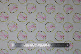 Flat swatch Bunny Wreath fabric (white fabric with repeated pattern pink drawn style bunnies in circular wreath badges made of yellow, rust and navy greenery/leaves and hearts)