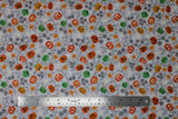Flat swatch Light Grey fabric (light grey fabric with tossed orange, yellow and green jack-o-lanterns in various styles/faces with grey leaves and vines, orange flowers and white stars)
