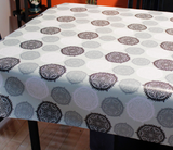Black Oval (stylized circular motifs with a central pointy flower design repeated in black, grey, and white on a pale green background) opaque vinyl draped over a dining room table with matching chairs around it.