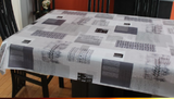 Grey decor (scattered rectangles of various grey and white textures overlap each other, all arranged parallel to the edges) opaque vinyl draped over a dining room table with matching chairs around it.