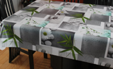 Grey Rain & Flowers (grey blocks sprinkled with turquoise water droplets arranged with branches of long, narrow leaves, daisies, smooth off-white stones, and turquoise stones, all on a white background, all giving the impression of a zen spa) opaque vinyl draped over a dining room table with matching chairs around it.