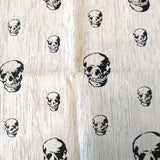 Jacquard upholstery fabric with stylized black skulls of varying sizes scattered on a white background