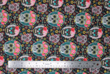 Flat swatch Craneo fabric (black fabric with small yellow, blue, white and red flowers allover and assorted sugar skulls in white and black tossed, some wearing pink flower crowns and behind either white or teal oval frames)