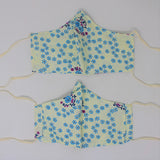 Front and back view of ninja style mask with off white elastic ear loops (off white mask with small blue floral heads allover and occasional purple floral swirls)