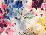 Slightly velvety white upholstery fabric printed with watercolour style abstract floral designs in the colourway Pinks/Blue/Yellow (pink, violet, royal blue, and yellow flowers with green leaves and dark brown branches or stems)