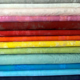 A stack of fabric bolts in a rainbow of colours, each with a faded or distressed grunge pattern.