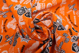 Swirled swatch of assorted Friday the 13th pattern on orange (bright medium orange fabric with multi emblems tossed in black and white. Crossing checkered flags, 13 badges, "Port Dover Motorcycle Rally" text, wheels, etc.)
