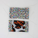 Front and back view of mask with white elastic ear loops (white mask with grey, yellow, orange, red, blue and green nails tossed allover)