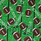 Square swatch touchdown fabric (green faux football field look fabric with black yard lines and tossed brown/white cartoon footballs allover and "Touchdown" "Tackle" etc. text in white tossed)