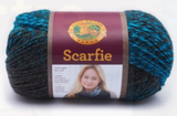 A ball of Lion Brand Scarfie on white background in shade charcoal aqua (dark grey and bright medium blue/green colourway)