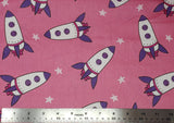 Flat swatch cartoon rocketships fabric in pink (dusty rose fabric with tossed cartoon rocket ships in white/purple/dark pink and tossed white stars)