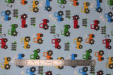 Flat swatch tractors fabric (pale light blue fabric with red, orange, green and blue cartoon tractors allover with small white cloud exhaust and grey picket fence sections)