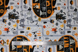 Flat swatch Halloween town fabric (white fabric with grey road look lines allover and Halloween themed town graphics allover: black castle look buildings, tombstones, ghosts, skeletons, etc. all in a white, grey, black, orange colourway)