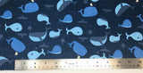 Flat swatch cartoon whales fabric in blue (dark blue fabric with tossed light blue cartoon whales and waves, tails, starfish, etc.)