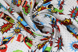 Swirled swatch of cartoon superhero print pattern in primary colours (white fabric with grey polka dots, cartoon superhero characters in blue, green, yellow and red colourway with comic book style words and logos "POW!" etc)