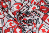 Swirled swatch Canadian signs white fabric (white fabric with tossed collaged Canadian badges and signs in white, red, black, grey with "Canada", flags, Highway 1, etc.)