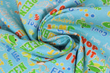 Swirled swatch toadally cool glow print fabric (light blue/aqua fabric with tossed frogs/toads in green and orange with primary coloured frog related text "Hop to it" "Green" etc.)