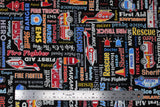 Flat swatch emergency services themed print fabric in first responders (black fabric with multi-coloured emergency related text "Rescue" "First Aid" etc and emergency vehicles)