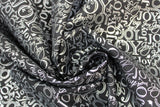 Swirled swatch Silver Joy fabric (black fabric with collaged "JOY" text allover in silver metallic, text has many different fonts and sizes and goes both horizontally and vertically)