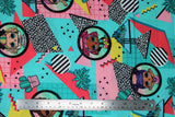 Flat swatch LOL Surprise Totally Awesome fabric (pink, teal, yellow fabric with geometric and random designs allover with black circular badges with full colour LOL characters within)