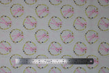 Flat swatch Bunny Wreath fabric (white fabric with repeated pattern pink drawn style bunnies in circular wreath badges made of yellow, rust and navy greenery/leaves and hearts)