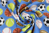 Swirled swatch of assorted sports balls fabric on blue (medium blue fabric with small tossed soccer, tennis, baseball, football, basketball)