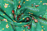 Swirled swatch hogwarts holiday fabric (green fabric with cartoon/kawaii style Ron, Harry, Hermione characters in front of Christmas tree text below in yellow and white reading "I'll stay at Hogwarts this Christmas" repeated pattern, tossed snowflakes, tossed yellow shield look badges with black cursive "H" within)
