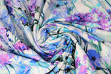 Swirled swatch Garden Bliss: Lily fabric (white fabric with busy collaged/tossed shades of blue and purple monochromatic floral and stems allover)