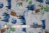 Flat swatch dusty blue/silver fabric (white fabric with tossed blue forest tree lines, blue moons, white and brown barn owls, green tree sprigs, white and green floral all with a snowy look and subtle silver sparkle)