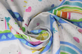 Swirled swatch when it rains fabric (white fabric with thick picture space between medium blue stripes with light blue hearts, rainbows, hearts, flowers, suns, clouds within space and "When it rains look for rainbows" "Dream big" text all in fun colours/happy cartoon theme)