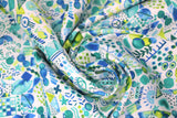 Swirled swatch of Marabella fabric in mallorca (white fabric with tiny blue, green, teal emblems collaged together allover: circles, eyes, fish, stars, etc.)