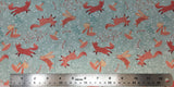 Flat swatch woodland fox and bunny printed fabric in green (faded green/blue fabric with tossed pink/orange cartoon foxes and bunnies, pink mushrooms, white/pink/green floral and greenery designs)