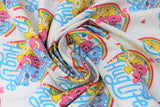 Swirled swatch care bear printed fabric in hug life (white fabric with repeated design of yellow, pink, blue care bears walking together with rainbow behind and blue "Hug Life" text in blue, tossed hearts in yellow and pink)