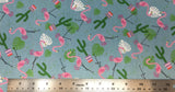 Flat swatch cartoon flamingos and cactus printed fabric in blue (faded blue fabric with tossed cartoon pink flamingos, white and green leaves, green cactus in pink planter)