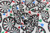 Swirled swatch man cave themed fabric in darts white (white fabric with tossed dart boards assorted sizes with red/blue/green darts)