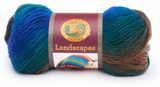 A ball of Lion Brand Landscapes yarn on white background in colourway skyline (bright medium blue, teal, brown, grey)