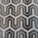 Woven upholstery fabric in a charcoal and cream geometric print. Cream shallow chevrons with posts extending out from each point, over charcoal. A thinner cream line traces the space between each offset row of chevrons