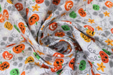 Swirled swatch Light Grey fabric (light grey fabric with tossed orange, yellow and green jack-o-lanterns in various styles/faces with grey leaves and vines, orange flowers and white stars)