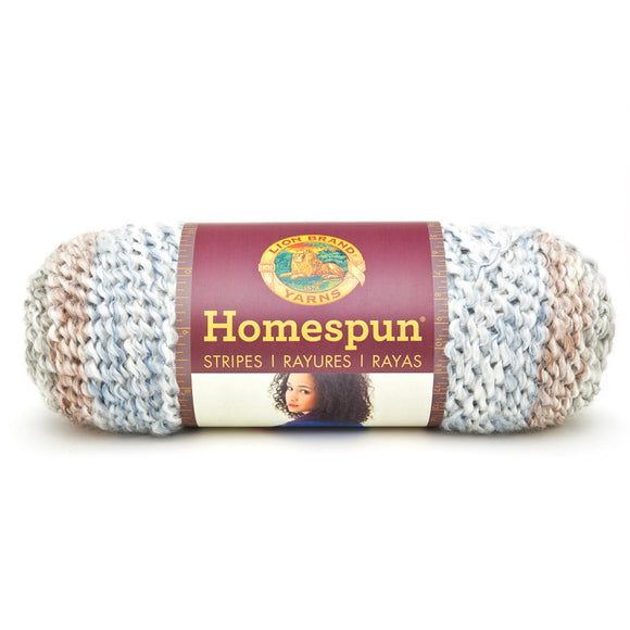 A ball of Lion Brand Homespun in a boucle texture and colourway Beachside Stripes (pale blue, white, sandy brown, light grey)