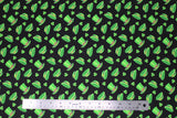 Flat swatch St. Patrick's Day themed fabric in green hats and shamrocks tossed on black