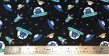 Flat swatch cartoon UFO and aliens printed fabric in black (black fabric with tossed blue cartoon aliens in small teal UFOs with tossed yellow and blue UFOs, teal rocketships, and tossed stars in various colours)
