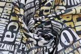 Swirled swatch journey themed fabric in large script (dark grey watercolour marbled fabric with white/yellow marbled look assorted size text with travel keywords "Trips" "Encounter" etc)