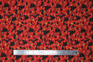 Square swatch Deck the Paws fabric (collaged drawn style poinsettia floral heads in red with yellow centers, and black cat heads in spaces with wide yellow and black eyes)