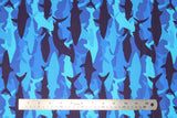 Flat swatch medium blue fabric with light to dark blue shark silhouettes in camo style design