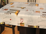 NY Taxi (scattered phrasing such as "N.Y." and "TAXI" in red, light grey, and taupe print scattered with New York scenes, yellow taxis, and traffic lights, all on an off-white background) opaque vinyl draped over a dining room table with matching chairs around it.