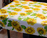Sunflowers (bright, large sunflowers with a few leaves over a bright white background) opaque vinyl draped over a dining room table with matching chairs around it.