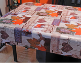 Wildlife (deer and foxes scattered among orange maple leaves, wrought iron decorative elements, bark textured hearts, and other rustic decor motifs, over off-white background) opaque vinyl draped over a dining room table with matching chairs around it.